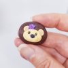 hand holding small brown pebble shape with hedgehog face and purple flower