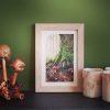 Framed painting of mossy tree and red toadstool on shelf against green wall to show art in situ